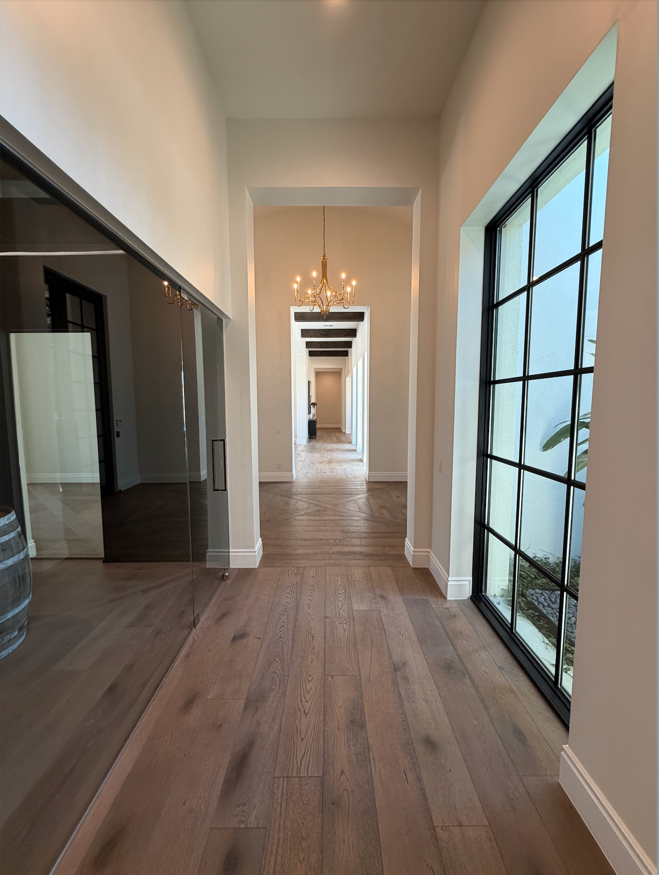 Elegant hallway with herringbone wood floors, steel-framed windows, and a custom chandelier